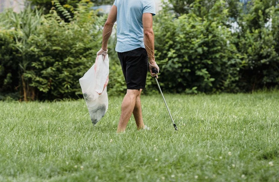 Man picking up litter in a park with the city skyline in the background, promoting environmental conservation.